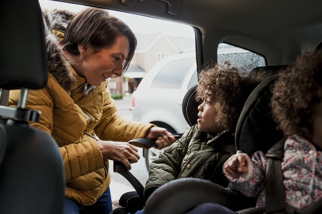A parent buckling their children into their car seats.