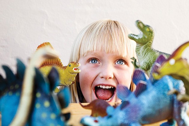 Child smiling next to plastic dinosaur figurines.