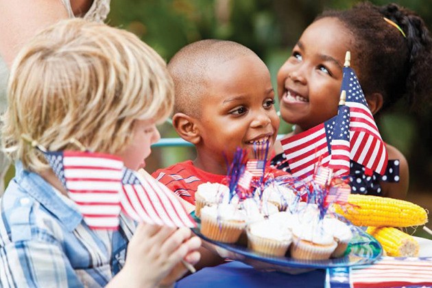 Kids eating cupcakes and holding American flags.