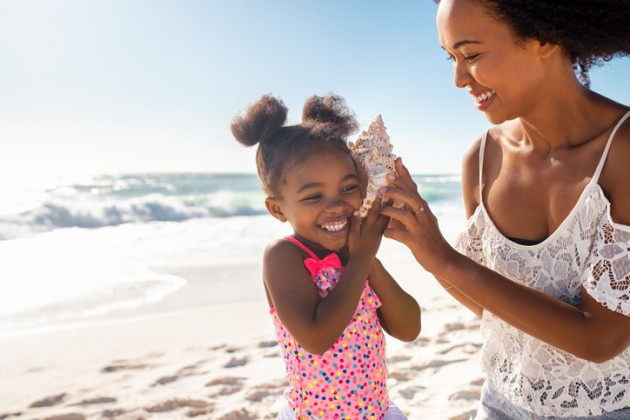 Little girl listening to a shell on the beach with her mom.
