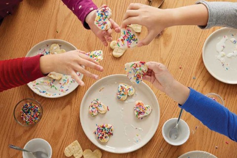 Kids decorating heart-shaped cookies with icing and sprinkles.